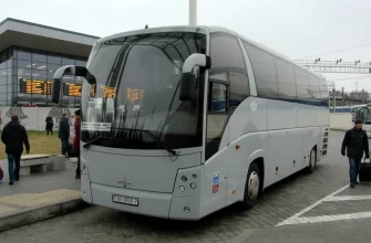 Светло-серый туристический автобус марки "МАЗ", принадлежащий ГП "Минсктранс" стоит на стоянке недалеко от стеклянного здания автовокзала.