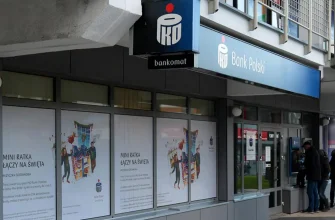 Внешний вид отделения PKO Bank Polski с банкоматом и вывеской. На окнах отделения размещены тематические рекламные плакаты.