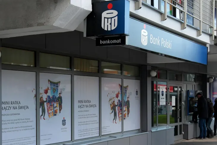 Внешний вид отделения PKO Bank Polski с банкоматом и вывеской. На окнах отделения размещены тематические рекламные плакаты.