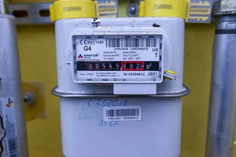 Крупный план бытового газового счетчика G4 с цифровым дисплеем, показывающим текущее потребление газа в кубических метрах, на фоне желтой стены.