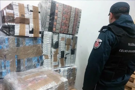 Сотрудник Таможенно-налоговой службы Польши стоит рядом с огромными штабелями изъятых нелегальных сигарет беларуского производства, упакованных в пленку.