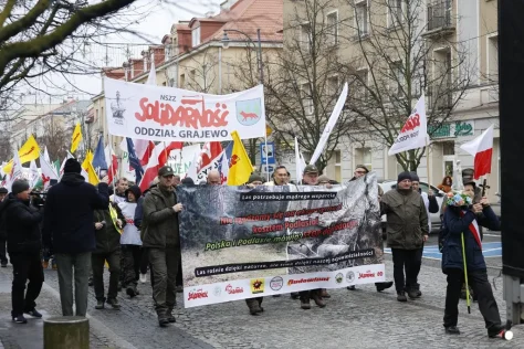 Участники манифестации в Белостоке в защиту Государственных лесов и лесопромышленного сектора несут большой транспарант с лозунгами о поддержке лесов и флаг профсоюза "Солидарность".