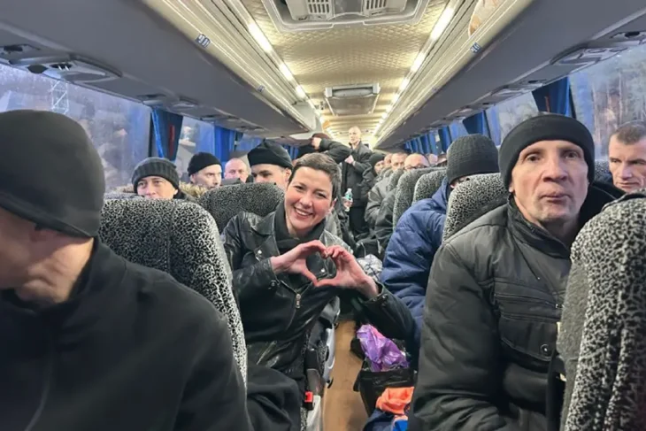 Мария Колесникова, одна из освобожденных политических заключенных, улыбается и показывает руками жест "сердце" среди других пассажиров в салоне автобуса, направляющегося из Беларуси.