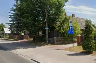 Уличный пейзаж в Белостоке, показывающий поворот на улицу ul. Kątowa, с дорожными знаками. На заднем плане — старый деревянный дом.