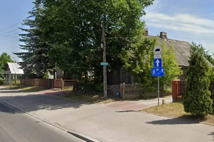 Уличный пейзаж в Белостоке, показывающий поворот на улицу ul. Kątowa, с дорожными знаками. На заднем плане — старый деревянный дом.