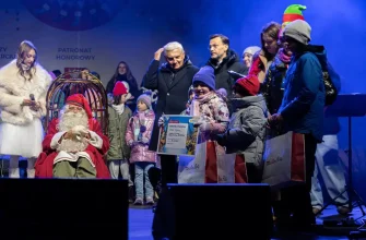 Сцена награждения или раздачи подарков: Санта-Клаус из Рованиеми сидит в кресле на сцене в Белостоке, а дети в зимней одежде получают призы и подарочные пакеты из рук организаторов.