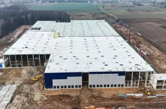 Аэроснимок строящегося логистического центра Panattoni Park Białystok III в Хороще (Choroszczy). Видно крупное одноэтажное здание склада с белой крышей и сине-серыми стенами, окруженное земляными работами.