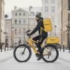 Курьер Glovo в Польше едет на велосипеде по заснеженной улице города.