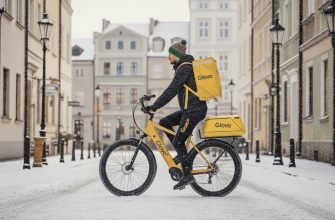 Курьер Glovo в Польше едет на велосипеде по заснеженной улице города.